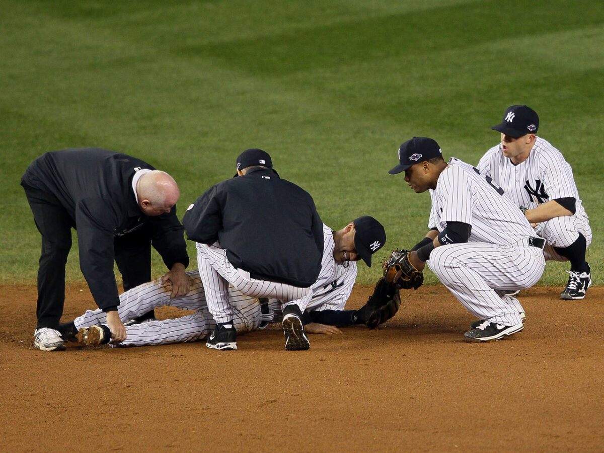 NEW YORK, NY - OCTOBER 13: Derek Jeter #2 of the New York Yankees is tended to by trainer Steve Donohue (L), manager Joe Girardi (C), Robinson Cano #24 and Brett Gardner #11 (R) of the New York Yankees after Jeter hurt his leg in the top of the 12th inning against the Detroit Tigers during Game One of the American League Championship Series at Yankee Stadium on October 13, 2012 in the Bronx borough of New York City, New York. (Photo by Alex Trautwig/Getty Images)